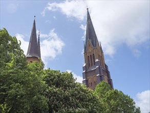 Church steeples towering over green trees in the cloudy sky, large church steeples with trees and