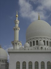 White shining mosque with several domes and high minarets under a blue sky, large mosque with white