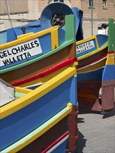 Several colourful boats on land with the inscriptions ANGEL CHARLES VALLETTA and ROCKY II VALLETTA,