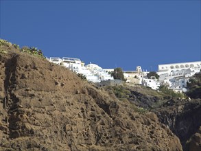 White buildings on rocky hills under a clear blue sky, rocky island in the sea with white houses