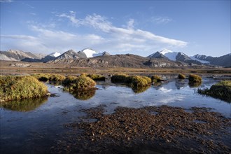 Mountain peaks reflected in a mountain lake, autumnal plateau with brown grass, glaciated and