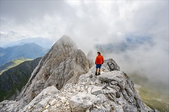 Mountaineer on a rocky narrow summit ridge, cloudy mountain peak, summit of the Great Kinigat,