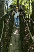 Sporty woman, tourist with camera in treetop path, suspension bridges, ropes, nets, beech forest,