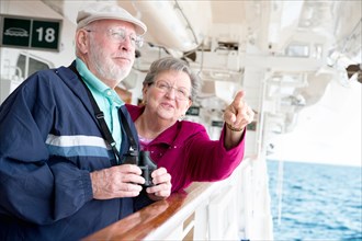 Senior adult couple enjoying the view from their passenger cruise ship with their bonoculars