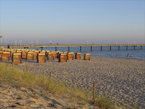 A quiet beach at sunset with beach chairs, a jetty and calm sea under a clear sky, many beach