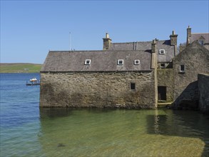 Old stone house on the clear blue water with a bright blue sky and a view of the coast, old stone