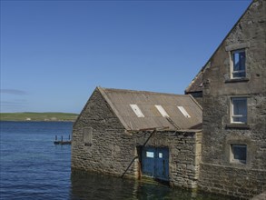 Old stone house with a blue Tor tor by the water, coastal landscape with blue sky, old stone house