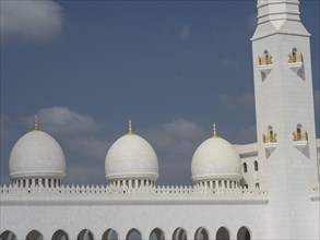 White minaret and domes of the mosque with golden decorations under a blue sky, beautiful mosque