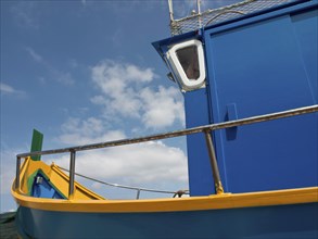 Close-up of a blue and yellow boat with clear sky and few clouds in the background, many colourful