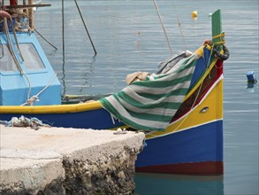 Small colourful boat moored at the pier, covered with a striped cloth, many colourful fishing boats