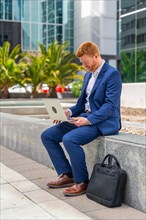Vertical photo of a businessman working with laptop sitting outside a financial building in the