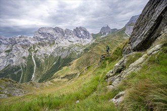 Mountaineer on a narrow hiking trail on a steep meadow slope, descent from the Raudenspitze, view