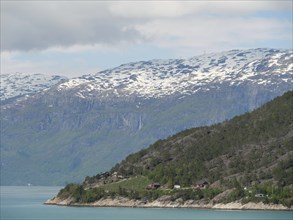 Fjord landscape with snow-capped mountains in the background and huts on the shore, spring