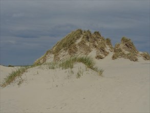 Hilly sand dunes with grass under a cloudy sky, secluded and quiet, dunes on an island with a blue