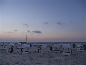 A calm dusk on a beach with white beach chairs and a soft sky, setting sun on a beach with beach