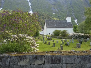 Small cemetery in front of a church with mountains in the background and flowering trees and