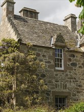 A historic stone house surrounded by a lush green garden and shrubs on a sunny day, old stone house