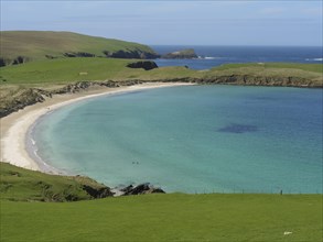A scenic panorama with a wide, peaceful sandy beach surrounded by green meadows and turquoise blue