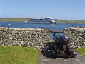 A cannon behind a wall with a view of a cruise ship in the sea, old cannons on a stone wall by the