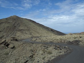 Winding road through a volcanic rocky landscape under a blue sky, barren landscape of lava