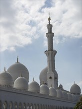 A towering minaret and several domes of the mosque shimmer against a slightly cloudy sky, large