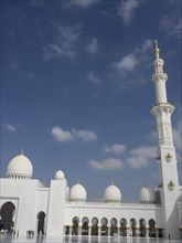 Majestic mosque with minaret, white domes and golden decorations under a bright blue sky, beautiful