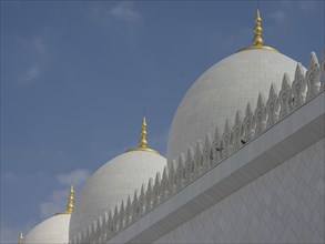 Close-up of white domes with golden spires against a blue sky, beautiful mosque with white domes