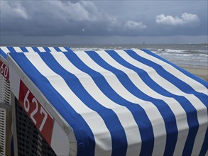 Close-up of blue and white beach chairs on the beach with the sea and a cloudy sky in the