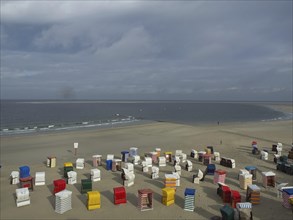 Colourful beach chairs are spread over the sandy beach, the sea and clouds can be seen in the