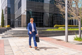 Businessman carrying laptop bag walking along city next to financial building