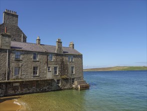 Old stone building on the waterfront with clear skies and calm sea in the background, calm sea with