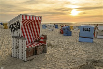 A red and white beach chair at sunset surrounded by other colourful beach chairs on the sandy