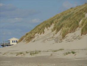 View of grassy sand dunes with a small house in the background, clouds on the beach with dunes by