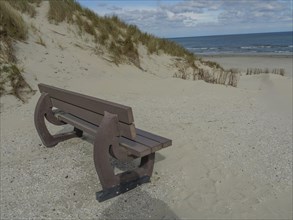 Beach scene with a wooden bench, dunes and sea under a cloudy sky, dunes on an island with a blue