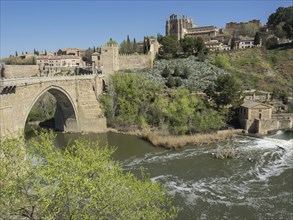 River with historic stone bridge and green vegetation in the background on a clear sunny day,