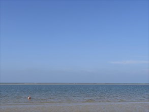 Clear sea water and an endless horizon under a light blue sky, calm and peaceful, dunes and beach