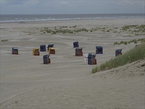 Abandoned beach chairs are scattered on the sandy beach in front of a cloudy coastline, colourful