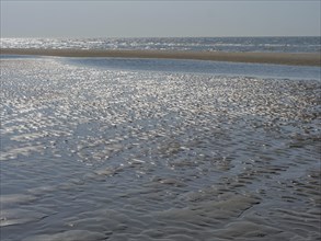 Extensive beach with textured sand surface and sparkling water, sparkling sea water at low tide on