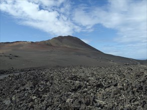 Vast desert landscape with volcano in the background and blue sky, barren landscape of lava