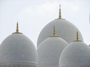 Large white domes of a mosque with golden spires against a sunny sky, beautiful mosque with white