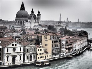 A foggy city view of Venice with many historic buildings along the canal, church towers and