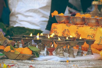 Close up to lit brass ghee lamps or butter lamps and sacred marigold flowers offering during