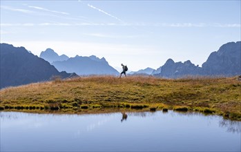 Mountaineer reflected in lake in front of mountain landscape, mountain lake and silhouettes of