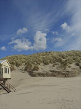 Small house on the edge of a sand dune under a clear sky with few clouds, clouds on the beach with