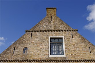 Close-up of a rustic brick house gable with a window under a bright blue sky, historic houses and a