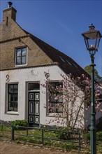 House with white walls, a lamp and a blossoming tree in spring, blue sky, historic houses in a