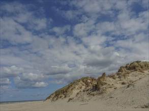 Sand dunes under a clear blue sky with scattered clouds on a sunny day, beach and dunes with grass