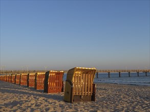 Beach chairs along the beach at sunset with a pier extending into the sea, beach chairs in the