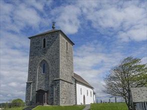 Stone church tower with a white nave, surrounded by green nature and clear sky, old stone church