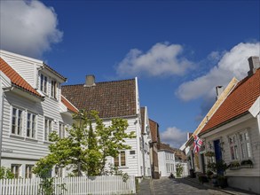 White houses with tiled roofs, plants and fence along a cobblestone street under a blue sky, white